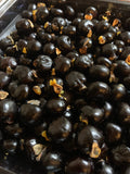 Close-up of bulk Blighia sapida (ackee) seeds in a dark tray, showing glossy black rounded seeds with yellow aril remnants, viewed from a slight angle
